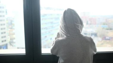 Kapüşonlu bir çocuğun pencereden dışarı bakışı..