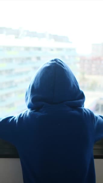 Вид Сзади Мальчика Капюшоне Выглядывающего Окна Городе — стоковое видео