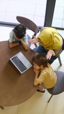 tesettürlü Müslüman anne ve çocukları, 5 ve 8, samimi bir Ramazan bayramı görüntüsü için bir dizüstü bilgisayarla bağlanıyorlar, teknolojiyle aralarındaki mesafeleri eşitliyorlar.