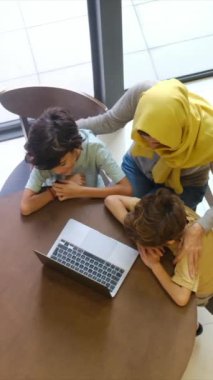 tesettürlü Müslüman anne ve çocukları, 5 ve 8, samimi bir Ramazan bayramı görüntüsü için bir dizüstü bilgisayarla bağlanıyorlar, teknolojiyle aralarındaki mesafeleri eşitliyorlar.