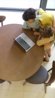 tesettürlü Müslüman anne ve çocukları, 5 ve 8, samimi bir Ramazan bayramı görüntüsü için bir dizüstü bilgisayarla bağlanıyorlar, teknolojiyle aralarındaki mesafeleri eşitliyorlar.
