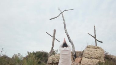 Dağlarda tahta haçların yanında dua eden bir kadın.
