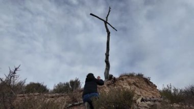 Dağlarda tahta haçın yanında dua eden bir kadın.