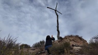 Dağlarda tahta haçın yanında dua eden bir kadın.