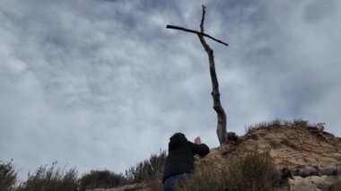 Dağlarda tahta haçın yanında dua eden bir kadın.