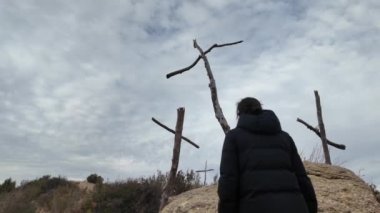 Dağlarda tahta haçların yanında dua eden bir kadın.