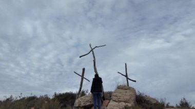 Dağlarda tahta haçların yanında dua eden bir kadın.