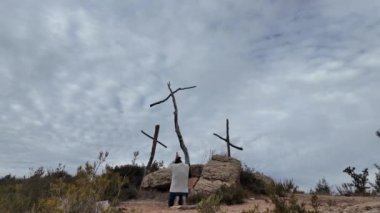 Dağlarda tahta haçların yanında dua eden bir kadın.