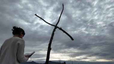 Dağlarda tahta haçın yanında dua eden bir kadın.