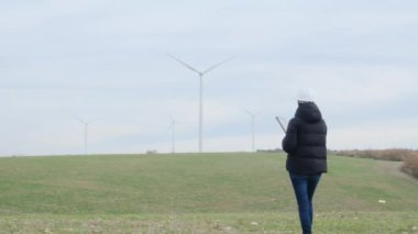 woman engineer with tablet  computer working in countryside with wind turbines