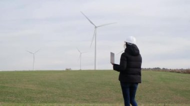 woman engineer with laptop computer working in countryside with wind turbines