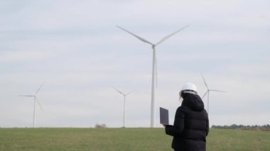 woman engineer with laptop computer working in countryside with wind turbines