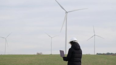 woman engineer with laptop computer working in countryside with wind turbines