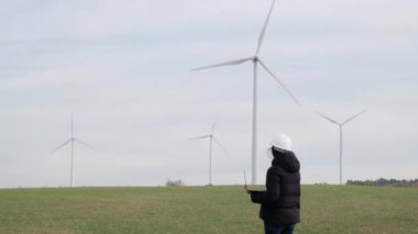 woman engineer with laptop computer working in countryside with wind turbines