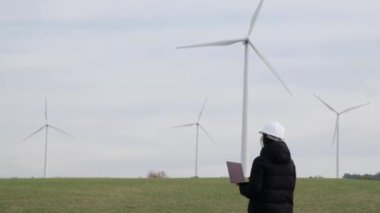 woman engineer with laptop computer working in countryside with wind turbines