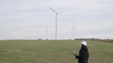 woman engineer with laptop computer working in countryside with wind turbines