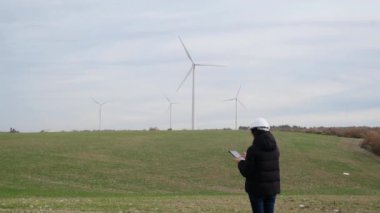 woman engineer with computer working in countryside with wind turbines