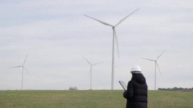 woman engineer with computer working in countryside with wind turbines