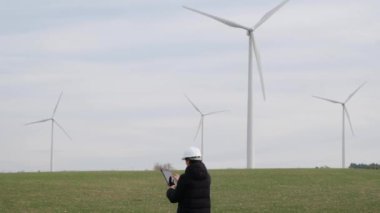 woman engineer with computer working in countryside with wind turbines