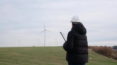 woman engineer with computer working in countryside with wind turbines