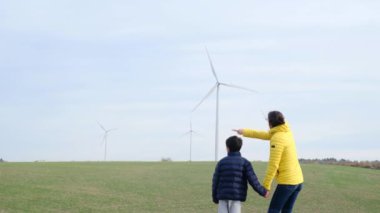 Anne ve oğlu kırsalda rüzgar türbinlerine bakıyor, ekoloji kavramı.