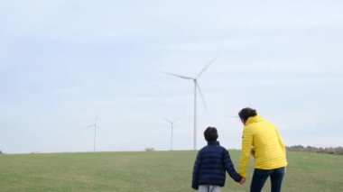 Anne ve oğlu kırsalda rüzgar türbinlerine bakıyor, ekoloji kavramı.