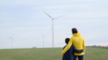 Anne ve oğlu kırsalda rüzgar türbinlerine bakıyor, ekoloji kavramı.