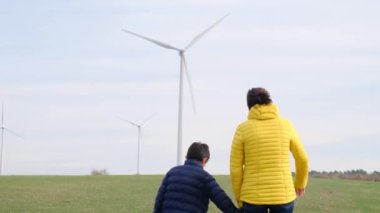 Anne ve oğlu kırsalda rüzgar türbinlerine bakıyor, ekoloji kavramı.