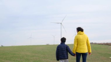 Anne ve oğlu kırsalda rüzgar türbinlerine bakıyor, ekoloji kavramı.