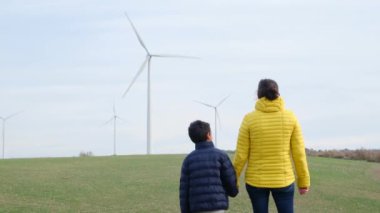 Anne ve oğlu kırsalda rüzgar türbinlerine bakıyor, ekoloji kavramı.