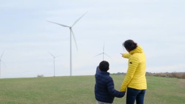Anne ve oğlu kırsalda rüzgar türbinlerine bakıyor, ekoloji kavramı.