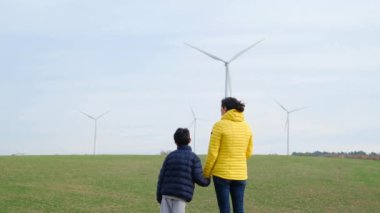 Anne ve oğlu kırsalda rüzgar türbinlerine bakıyor, ekoloji kavramı.