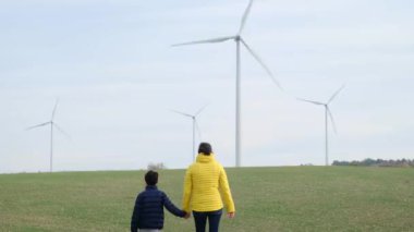 Anne ve oğlu kırsalda rüzgar türbinlerine bakıyor, ekoloji kavramı.