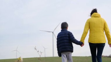 Anne ve oğlu kırsalda rüzgar türbinlerine bakıyor, ekoloji kavramı.