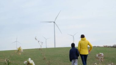 Anne ve oğlu kırsalda rüzgar türbinlerine bakıyor, ekoloji kavramı.