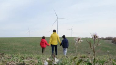 Oğulları olan bir anne kırsalda rüzgar türbinleriyle yürüyor, ekoloji kavramı.