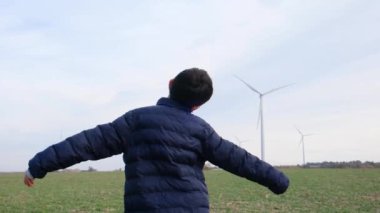 Kırsal kesime uzanmış çocuk rüzgar türbinlerine bakıyor, ekoloji kavramı.
