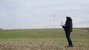 woman engineer with laptop computer working in countryside with wind turbines