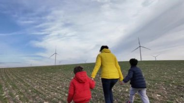 Oğulları olan bir anne kırsalda rüzgar türbinleriyle yürüyor, ekoloji kavramı.