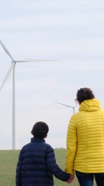 Anne ve oğlu kırsalda rüzgar türbinlerine bakıyor, ekoloji kavramı.