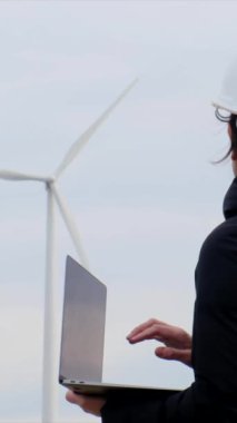woman engineer with laptop computer working in countryside with wind turbines
