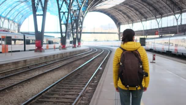 バックパック付きの若い女性旅行者は プラットフォーム上の列車を待っています — ストック動画