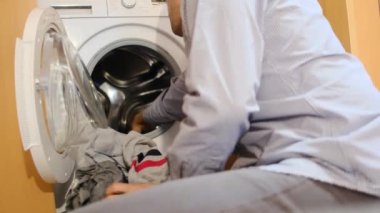 Çamaşır makinesine çamaşır koyan adam.