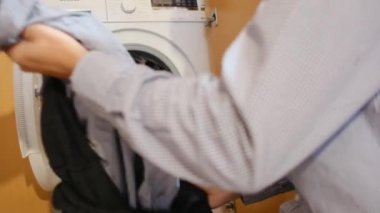 Çamaşır makinesinde çocukların çamaşırlarını yıkayan bir adam. Cinsiyet ve ev işleri, eşitlik kavramlarını bir kenara bırak ve bir adamın evde ailesine ve karısına yardım et..