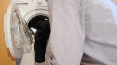 Çamaşır makinesine çamaşır koyan adam.
