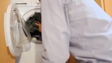 Çamaşır makinesine çamaşır koyan adam.