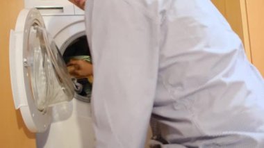 Çamaşır makinesinde çocukların çamaşırlarını yıkayan bir adam. Cinsiyet ve ev işleri, eşitlik kavramlarını bir kenara bırak ve bir adamın evde ailesine ve karısına yardım et..