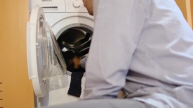 Çamaşır makinesinde çocukların çamaşırlarını yıkayan bir adam. Cinsiyet ve ev işleri, eşitlik kavramlarını bir kenara bırak ve bir adamın evde ailesine ve karısına yardım et..