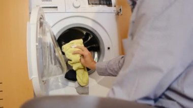 Çamaşır makinesinde çocukların çamaşırlarını yıkayan bir adam. Cinsiyet ve ev işleri, eşitlik kavramlarını bir kenara bırak ve bir adamın evde ailesine ve karısına yardım et..