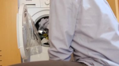 Çamaşır makinesinde çocukların çamaşırlarını yıkayan bir adam. Cinsiyet ve ev işleri, eşitlik kavramlarını bir kenara bırak ve bir adamın evde ailesine ve karısına yardım et..